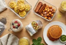 Flat lay photograph of high protein vegan breakfast meal prep on a wooden counter, showing tofu burritos, chickpea muffins, tempeh sweet potato hash, savory red lentil pancakes, and overnight oats without eggs.
