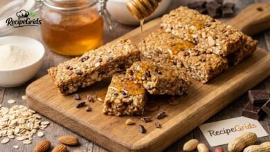 A stack of homemade stars and honey protein bars drizzled with raw honey on a wooden cutting board, surrounded by healthy ingredients like oats and almonds.