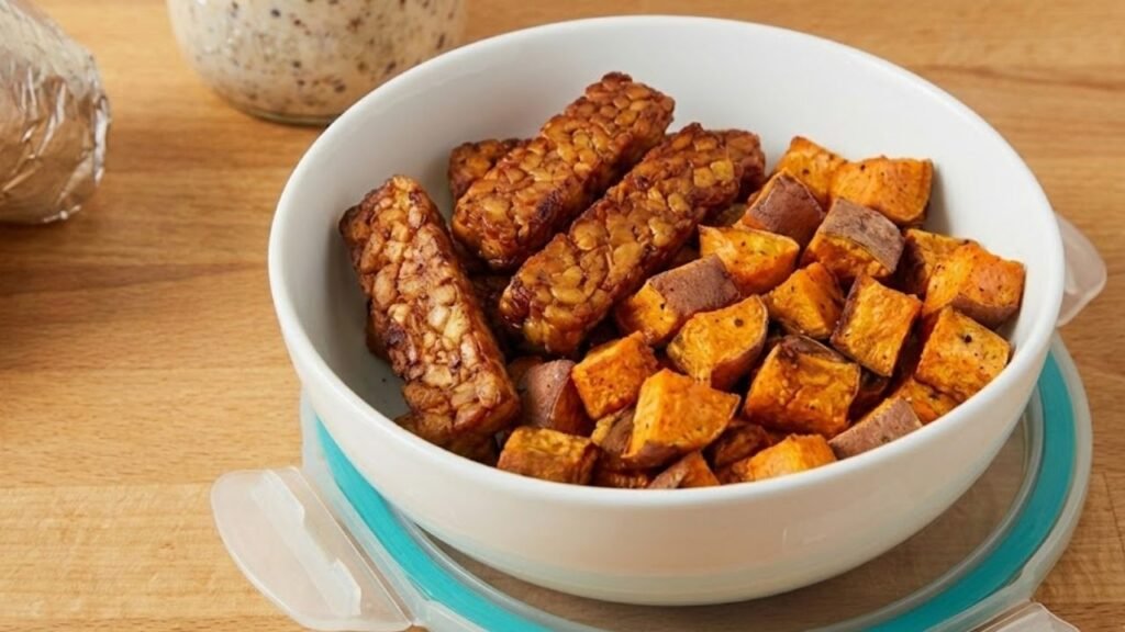 A white bowl filled with cubed roasted sweet potatoes and golden-brown strips of tempeh.