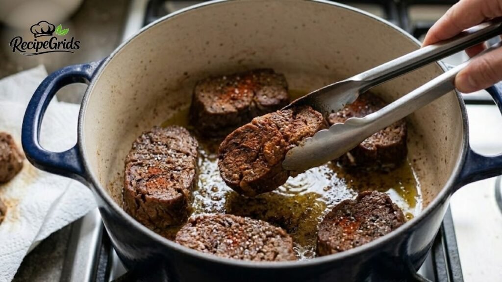 Hand using metal tongs to flip seasoned vegan mock chuck as it sears in a hot blue Dutch oven.