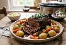A tender slow cooker rump roast recipe served on a rustic platter with baby potatoes, carrots, and rich savory gravy, with a crock pot in the background.