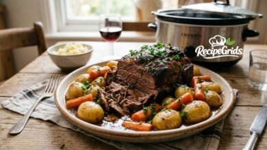 A tender slow cooker rump roast recipe served on a rustic platter with baby potatoes, carrots, and rich savory gravy, with a crock pot in the background.
