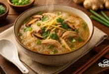 Chicken long rice recipe served in a bowl with shredded chicken, glass noodles, shiitake mushrooms, and ginger broth garnished with green onions
