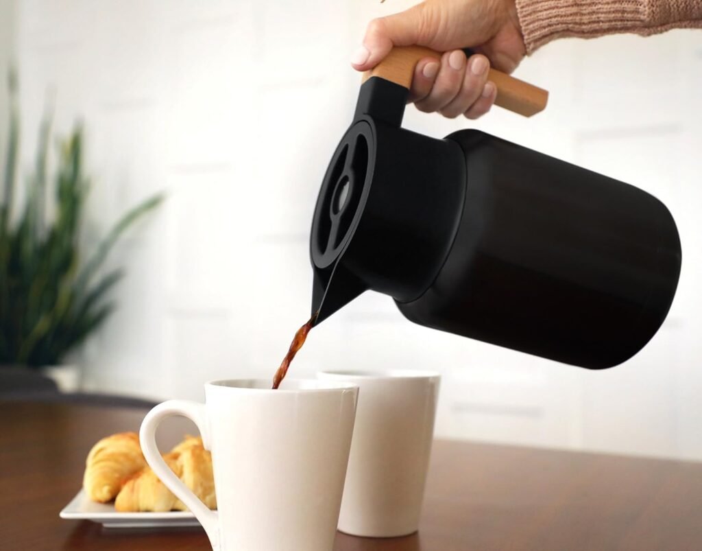 Hastings Collective Large Thermal Carafe with a minimalist matte black design and wood handle, pouring coffee into white mugs next to fresh croissants.