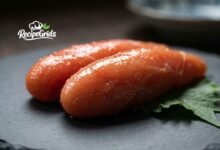 Close-up of fresh, spicy Mentaiko (Japanese pollock roe) resting on a shiso leaf over a dark slate plate, by RecipeGrids.