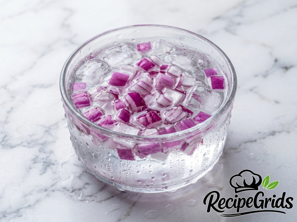 Diced red onions soaking in a glass bowl filled with ice water to reduce their sharp bite.